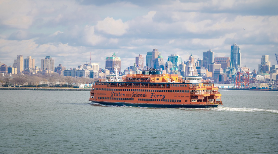 Orange Staten Island Ferry in the Hudson with Manhattan skyline in the background.